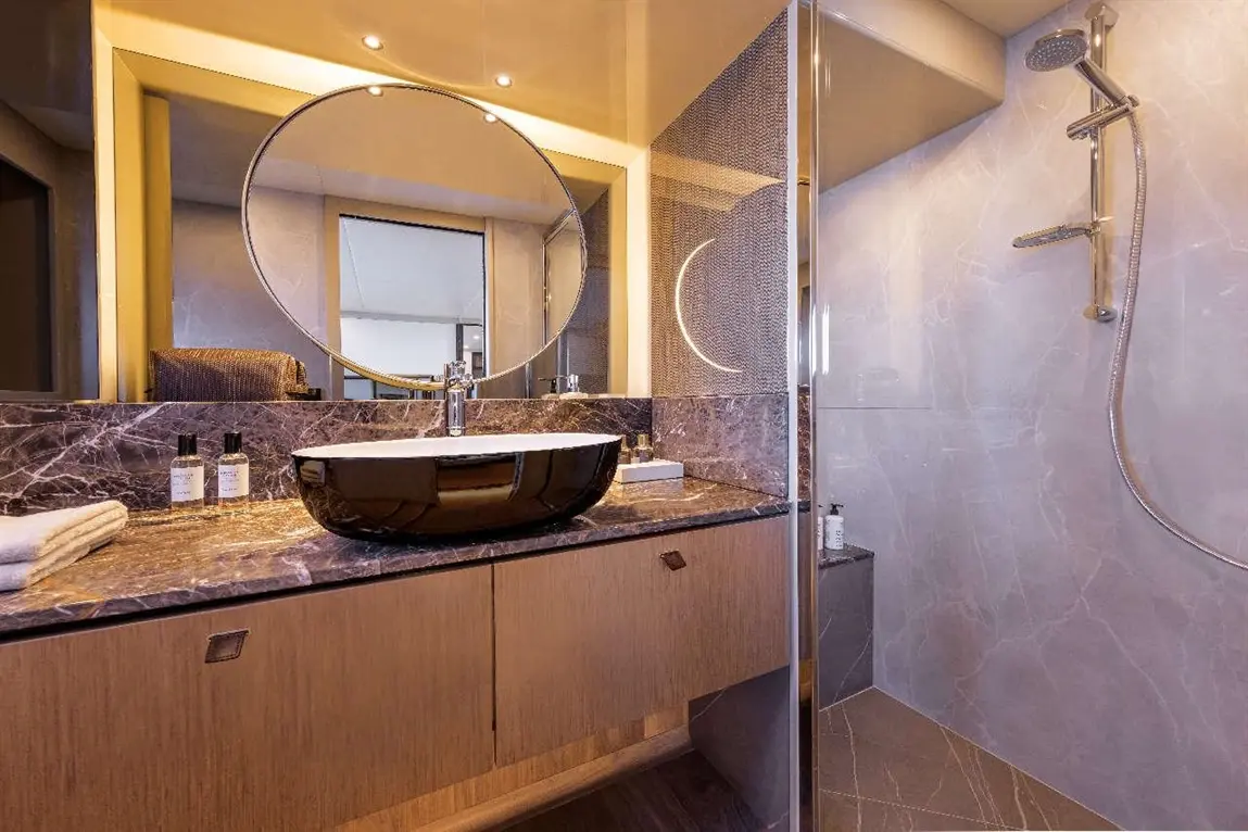 Modern bathroom featuring a round mirror, sleek basin, and stylish shower, complemented by luxury toiletries on a marble countertop.